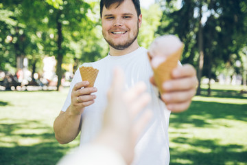 man giving ice cream in hot sunny day in city park. first person point of view reach out hand