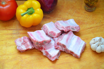 Raw uncooked pork ribs on a paper on dark brown wooden background. Ingredients for meat raw pork ribs sage, thyme, rosemary, pepper, basil, salt.