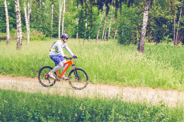 Naklejka premium A cyclist in a helmet rides through the forest on a bicycle path