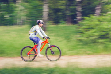 Naklejka premium A cyclist in a helmet rides through the forest on a bicycle path, motion blur