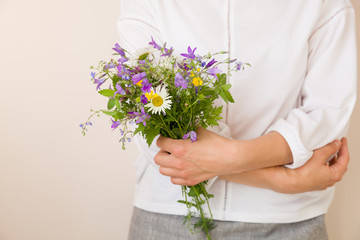 Closeup of woman's hands holding beautiful bunch of wild flowers. Girl with summer bouquet at white wall