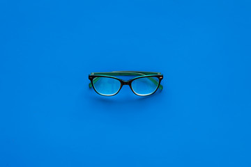 One glasses with transparent lenses on blue background top view copy space