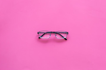 One glasses with transparent lenses on pink background top view copy space