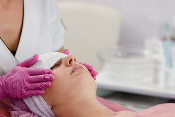Professional dermatologist using cosmetician napkin to clean female face