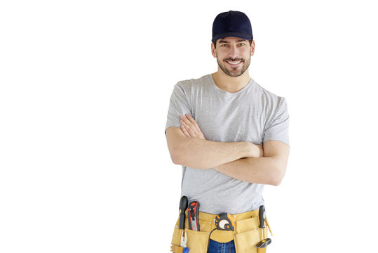 Portrait of young handyman standing at isolated white background with copy space. Successful repairman wearing baseball cap and tool belt.