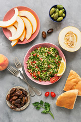 Lebanese traditional dish, the salad of parsley and bulgur tabbouleh on a gray concrete background. Different Eastern or Arabic food , melon,peach,dates,olives. flat lay