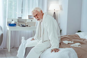 Total exhaustion. Weary senior man sitting on bed and looking at camera