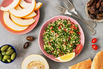 tabbouleh salad and various middle Eastern or Arabic food , melon,peach,date,olives on grey...