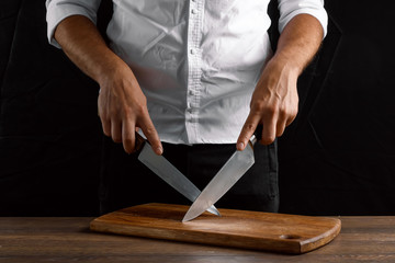 Hands of the chef close-up with a knife and a wooden board on a dark background. The concept of cooking, cooking, recipe dishes.