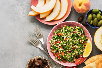 Tabbouleh or Parsley salad on pink platter, easy and healthy classic vegetarian dish with bulgur, tomatoes, parsley, spring onion and mint, olive oil on grey background. Top view, space for text.