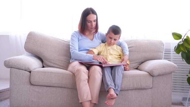 Mother and her son reading book while sitting in armchair on sunny day