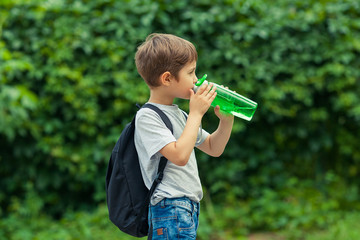 Little boy drinking water from a bottle, hot summer. Child is traveling with a backpack. Vacation in the woods.