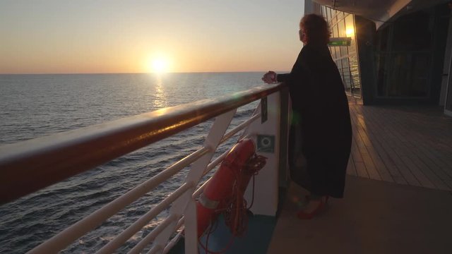 Woman passenger stands on cruise ship deck at sunset - midnight sun