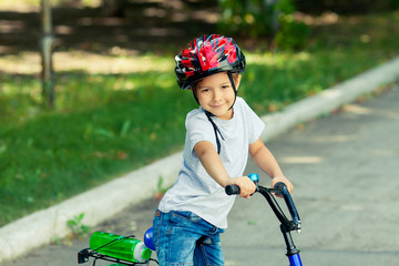 Obraz premium Little boy learns to ride a bike in the park near the home. Portrait of a cute kid on bicycle. Happy smiling child in helmet riding a cycling.