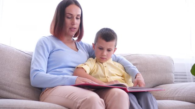 Mother sitting on couch and reading book with son