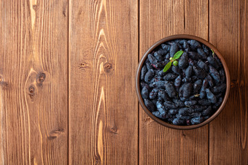 Honeysuckle berries or Lonicera caerulea in ceramic bowl on wooden background