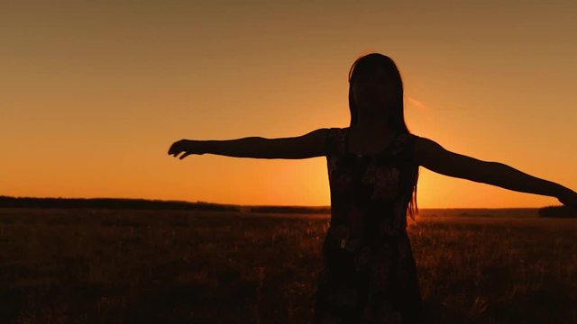 Girl with long hair whirls in flight under rays of golden sunset. Free woman on an evening walk playing in field. Slow motion.