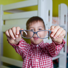 Little boy holds in his hands the glasses. Kid has poor vision. Child examines your eyes...