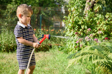 Cute little boy watering the garden with hose.