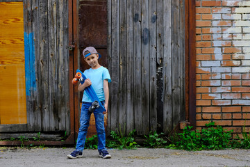 Beautiful young boy standing with a skateboard, against the background of the urban wall. Children ride on the Board in the street. Active lifestyle, sports, training, fresh air.