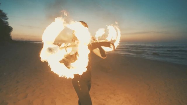 Young man in a mask of a predator shows a fire show on the beach.