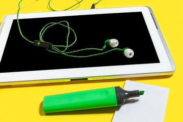 set of business or education accessories. green pencils, headphones, paper stickers, opened marker and tablet pc lying on a yellow background. concept of the office gadgets and chancery