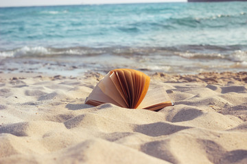 Fototapeta na wymiar An open book laying on a sandy sunny beach at sunset.