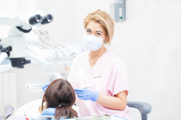 Fototapeta premium A female dentist is treating a girl's teeth with a brunette. Doctor in gloves, mask and goggles