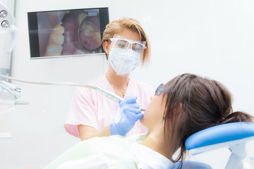 Fototapeta na wymiar A female dentist is treating a girl's teeth with a brunette. Doctor in gloves, mask and goggles