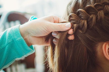 The hairdresser plaits the braid girl. Hands, close-up. Pretty haircut. - obrazy, fototapety, plakaty