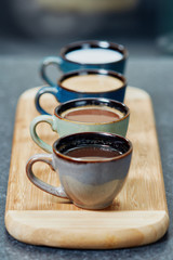 Four coffee cups in a row on a wooden bar displaying different mixtures of milk and coffee