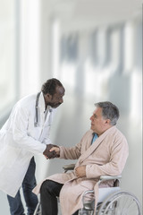 African ,American,male doctor greeting recovering senior patient in wheelchair in hospital handshake