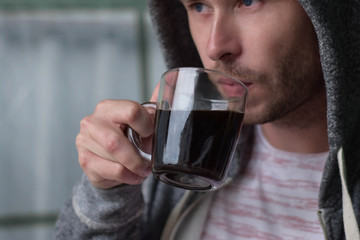 Young man drinks coffee. Man drinks coffee. Young man drinks coffee outdoor. Man drink coffee in cafe. Cozy atmosphere. Dramatic photography.