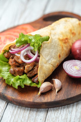 Doner kebab is lying on the cutting board. Shawarma with meat, onions, salad lies on a dark old wooden table.