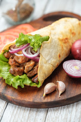 Doner kebab is lying on the cutting board. Shawarma with meat, onions, salad lies on a dark old wooden table.