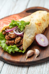 Doner kebab is lying on the cutting board. Shawarma with meat, onions, salad lies on a dark old wooden table.