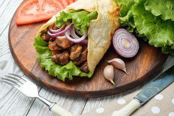 Doner kebab is lying on the cutting board. Shawarma with meat, onions, salad lies on a white old wooden table.
