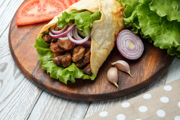 Doner kebab is lying on the cutting board. Shawarma with meat, onions, salad lies on a white old wooden table.