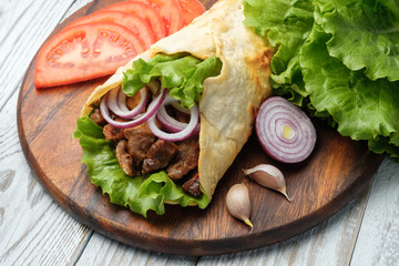 Doner kebab is lying on the cutting board. Shawarma with meat, onions, salad lies on a white old wooden table.