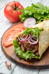 Doner kebab is lying on the cutting board. Shawarma with meat, onions, salad lies on a white old wooden table.