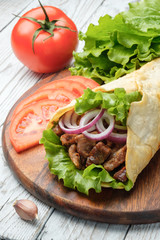 Doner kebab is lying on the cutting board. Shawarma with meat, onions, salad lies on a white old wooden table.