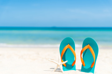 Beach accessories including flip flop, starfish and sea shell on sandy beach, green sea and blue...