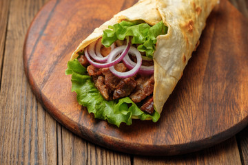 Doner kebab is lying on the cutting board. Shawarma with meat, onions, salad lies on a dark old wooden table.