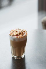 Latte macchiato with whipped creamand caramel on a wooden table in a coffee house. Selective focus, vertical composition