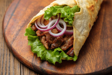 Doner kebab is lying on the cutting board. Shawarma with meat, onions, salad lies on a dark old wooden table.