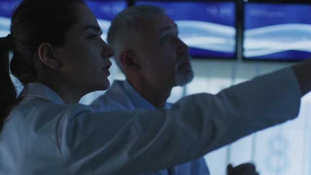Close-up Shot of Two Medical Scientists / Neurologists, Talking and Pointing at TV Wall Monitor in the  Modern Laboratory. Shot on RED EPIC-W 8K Helium Cinema Camera.