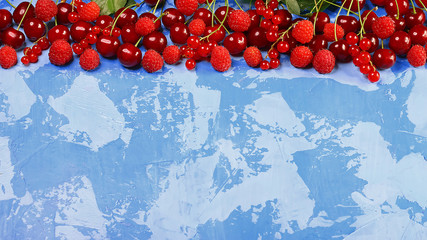 Red fruits and berries. Ripe red currants, strawberries, raspberries, cherries on a blue background. Berries at border of image with copy space. Top view