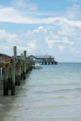 Old wooden pier with building, boat, calm sea, blue sky clouds.