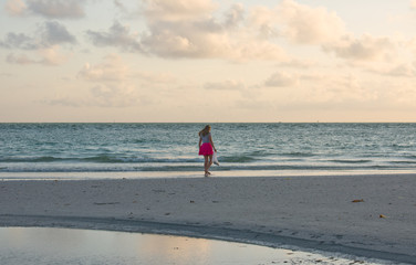 Girl on beach, pink skirt, collecting shells at sunset.
