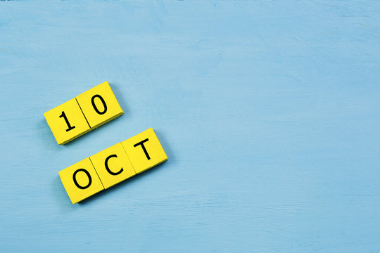OCT 10, yellow cube calendar on blue wooden surface with copy space